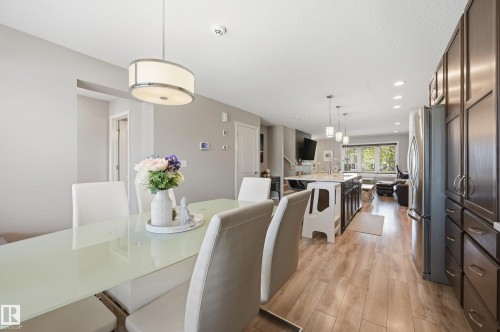 Open-concept living space featuring wood-finish flooring, a contemporary kitchen island with pendant lighting, dark wood cabinetry, and a stainless steel refrigerator - 3457 Cutler Crescent, Edmonton, AB - Indoor Photo Showing Dining Room