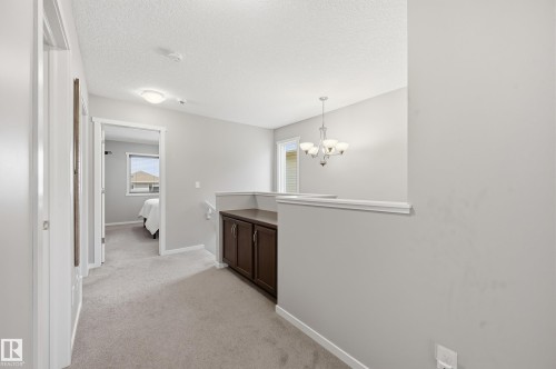 Carpeted hallway featuring light gray walls, white trim, a built-in dark wood cabinet with double doors, and a decorative chandelier - 3457 Cutler Crescent, Edmonton, AB - Indoor Photo Showing Other Room