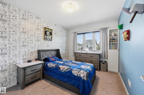 Carpeted room featuring a window with horizontal blinds, built-in shelving, and a wall adorned with patterned wallpaper - 3457 Cutler Crescent, Edmonton, AB - Indoor Photo Showing Bedroom