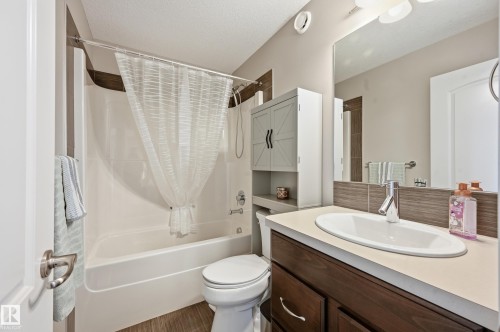Full bathroom featuring a white tub and shower combination, wood-finish flooring, dark wood-finish vanity with a light-toned countertop, and a built-in wall cabinet above the toilet - 3457 Cutler Crescent, Edmonton, AB - Indoor Photo Showing Bathroom