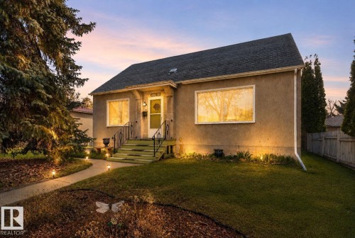 Stucco-sided home featuring a prominent front entrance with white trim, dark steps, and black railings - 11614 70 Street, Edmonton, AB 