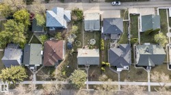 Residential street with multiple properties featuring mature trees, paved sidewalks, and diverse rooflines - 