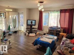 Living area featuring wood-finish flooring, white walls, and a modern multi-bulb ceiling fixture - 