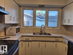 Kitchen featuring cream-colored cabinetry with decorative trim, a dual basin stainless steel sink with a high-arch faucet, a three-pane window, and a tiled backsplash - 