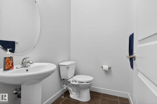 Pedestal sink with chrome faucet, oval wall mirror, and neutral wall paint - 11 450 Mcconachie Way, Edmonton, AB - Indoor Photo Showing Bathroom