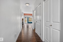 Brown square tile flooring defines a hallway with white paneled doors and walls - 