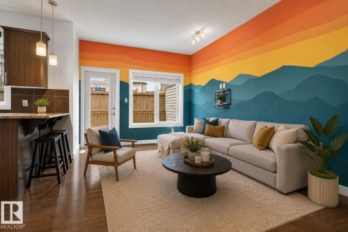 Open-concept living space featuring wood-finish flooring, a contemporary mountain-mural accent wall, and a large window providing outdoor illumination - 11 450 Mcconachie Way, Edmonton, AB - Indoor Photo Showing Living Room