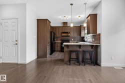 Open-concept kitchen featuring wood-finish cabinetry, black appliances, and a breakfast bar with pendant lighting - 