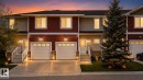 Multi-level townhome exterior featuring red and beige siding, a two-car garage with panel doors, and integrated outdoor lighting - 11 450 Mcconachie Way, Edmonton, AB  - Outdoor With Facade 