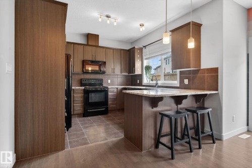 Kitchen featuring wood-finish cabinetry, black appliances, a tile backsplash, and a breakfast bar with stone-finish countertops - 11 450 Mcconachie Way, Edmonton, AB - Indoor Photo Showing Kitchen