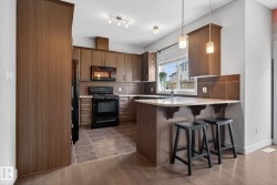 Kitchen featuring wood-finish cabinetry, black appliances, a tile backsplash, and a breakfast bar with stone-finish countertops - 