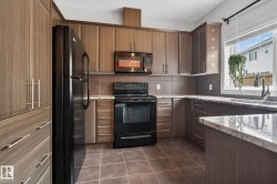 Kitchen featuring wood-finish cabinetry, black appliances, stone-look countertops, a tile backsplash, and tile flooring - 