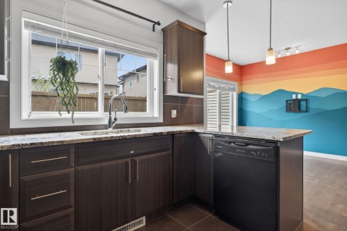 Kitchen featuring dark wood-finish cabinetry, light-toned granite countertops, a stainless steel faucet, and an integrated black dishwasher - 11 450 Mcconachie Way, Edmonton, AB - Indoor