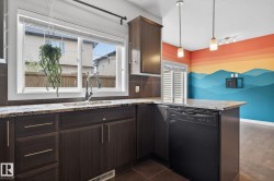 Kitchen featuring dark wood-finish cabinetry, light-toned granite countertops, a stainless steel faucet, and an integrated black dishwasher - 