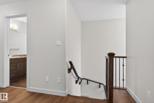 Hardwood-finish flooring extending from the hallway into the bathroom, featuring a dark wood newel post and black metal balusters - 11 450 Mcconachie Way, Edmonton, AB - Indoor Photo Showing Other Room