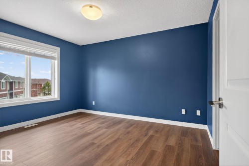 Inviting room featuring a large window, rich wood-finish flooring, vibrant blue walls, white trim, and a semi-flush ceiling light fixture - 11 450 Mcconachie Way, Edmonton, AB - Indoor Photo Showing Other Room