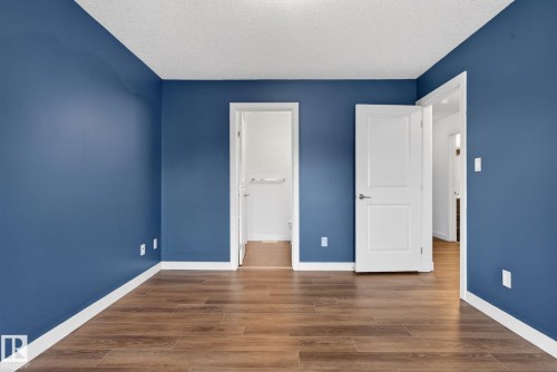 Interior room featuring rich blue wall paint, wood-finish flooring, white baseboards, and white two-panel interior doors - 11 450 Mcconachie Way, Edmonton, AB - Indoor Photo Showing Other Room