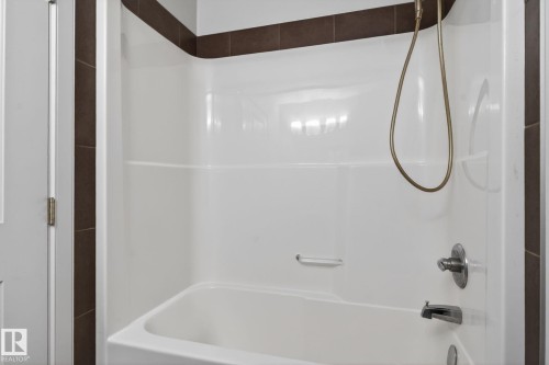 White tub-shower combination unit featuring integrated shelving, a brushed nickel faucet, and a handheld shower head - 11 450 Mcconachie Way, Edmonton, AB - Indoor Photo Showing Bathroom