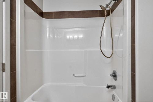 White bathtub and shower combination unit featuring a handheld showerhead with a bronze-finish hose and chrome fixtures - 11 450 Mcconachie Way, Edmonton, AB - Indoor Photo Showing Bathroom