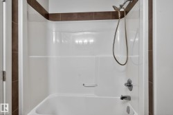 White bathtub and shower combination unit featuring a handheld showerhead with a bronze-finish hose and chrome fixtures - 
