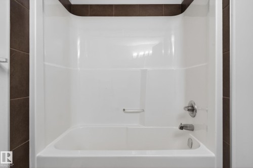 White acrylic tub and shower combination with chrome fixtures, complemented by dark brown tile surround - 11 450 Mcconachie Way, Edmonton, AB - Indoor Photo Showing Bathroom