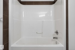 White acrylic tub and shower combination with chrome fixtures, complemented by dark brown tile surround - 