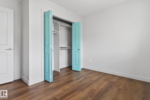 Bedroom featuring warm wood-finish flooring, white baseboards, a white interior door with a chrome handle, white walls, and a closet with bifold turquoise doors - 11 450 Mcconachie Way, Edmonton, AB - Indoor Photo Showing Other Room