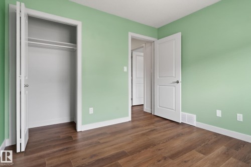 Room featuring wood-finish flooring, light green walls, white baseboards, and a white interior door - 11 450 Mcconachie Way, Edmonton, AB - Indoor Photo Showing Other Room