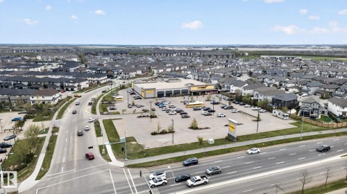 Aerial overview of a suburban community featuring a commercial center with ample parking, surrounded by residential properties with dark-pitched roofs - 11 450 Mcconachie Way, Edmonton, AB - Outdoor With View