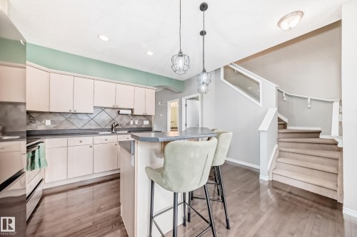 Kitchen featuring wood-finish flooring, light-toned cabinetry, a central island with a countertop, a tile backsplash, and recessed lighting - 105 13825 155 Avenue, Edmonton, AB - Indoor Photo Showing Kitchen With Upgraded Kitchen
