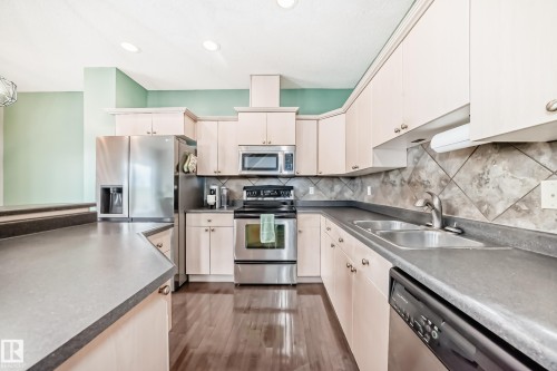 Spacious kitchen featuring light-toned cabinetry, stainless steel appliances, dark countertops, and wood-finish flooring - 105 13825 155 Avenue, Edmonton, AB - Indoor Photo Showing Kitchen With Stainless Steel Kitchen With Double Sink