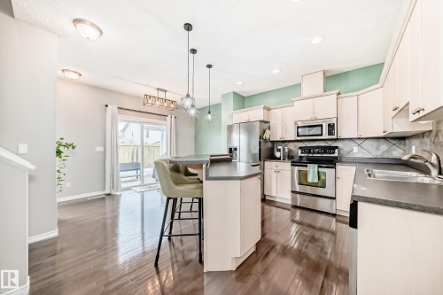 Kitchen featuring stainless steel appliances, dark countertops, light cabinetry, and a textured tile backsplash - 105 13825 155 Avenue, Edmonton, AB - Indoor Photo Showing Kitchen With Stainless Steel Kitchen