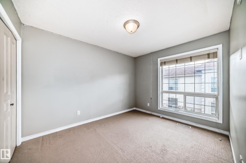 Carpeted room featuring a large window, a ceiling-mounted light fixture, white baseboards, and a bi-fold closet door - 105 13825 155 Avenue, Edmonton, AB - Indoor Photo Showing Other Room