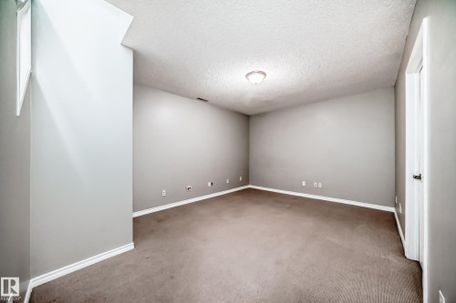 Spacious room featuring neutral grey walls, textured ceiling, and brown carpet flooring - 105 13825 155 Avenue, Edmonton, AB - Indoor Photo Showing Other Room