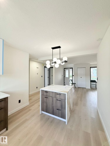 Modern kitchen island featuring a waterfall-edge countertop with veining, wood-finish cabinetry, and matte black hardware - 11628 151 Avenue Nw, Edmonton, AB 