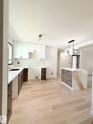 Contemporary kitchen featuring two-tone cabinetry, light wood-finish flooring, and a waterfall-edge island with a marble-look countertop - 11628 151 Avenue Nw, Edmonton, AB 