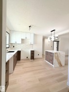 Contemporary kitchen featuring two-tone cabinetry, light wood-finish flooring, and a waterfall-edge island with a marble-look countertop - 