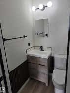 Bathroom featuring a wood-finish vanity with a white countertop and integrated sink, matte black faucet, and coordinating hardware - 