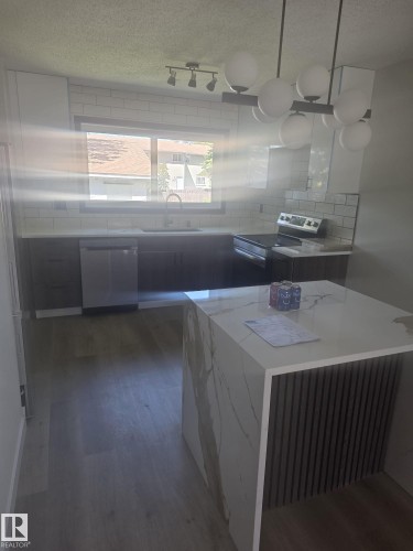 Modern kitchen featuring a waterfall island with a slatted base, wood-finish flooring, and white subway tile backsplash - 11628 151 Avenue Nw, Edmonton, AB 