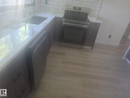 Kitchen featuring white stone-finish countertops, subway tile backsplash, stainless steel appliances, dark wood-finish cabinetry, and wood-finish flooring - 11628 151 Avenue Nw, Edmonton, AB 