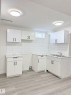 Kitchenette featuring white cabinetry, subway tile backsplash, a double basin stainless steel sink, and wood-finish flooring - 11628 151 Avenue Nw, Edmonton, AB 