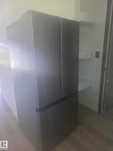 Stainless steel French door refrigerator with bottom freezer compartment, adjacent to white wall-mounted shelving - 11628 151 Avenue Nw, Edmonton, AB 