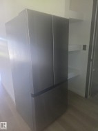 Stainless steel French door refrigerator with bottom freezer compartment, adjacent to white wall-mounted shelving - 