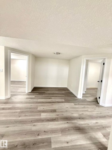 Spacious room featuring wood-finish flooring, white walls, and bright overhead lighting - 11628 151 Avenue Nw, Edmonton, AB 