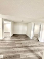 Spacious room featuring wood-finish flooring, white walls, and bright overhead lighting - 