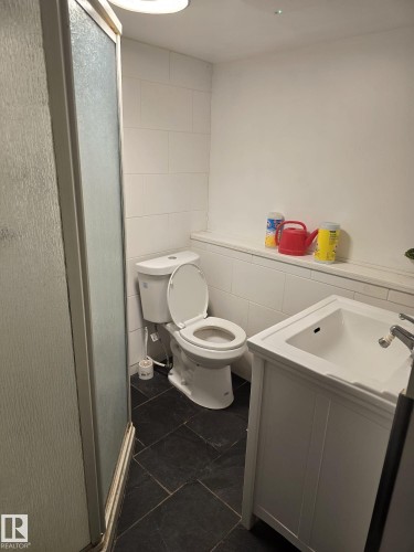 Bathroom featuring a walk-in shower with frosted glass enclosure, white square tile wainscoting, white toilet, and a white vanity with an integrated sink - 11927 85 Street Nw, Edmonton, AB - Indoor Photo Showing Bathroom