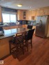 Kitchen featuring wood-finish flooring, light wood cabinetry, and a dark stone countertop with an integrated breakfast bar - 11927 85 Street Nw, Edmonton, AB  - Indoor 