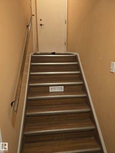 Staircase featuring wood-finish treads with metallic anti-slip strips, a light wood handrail, and a white interior door - 11927 85 Street Nw, Edmonton, AB - Indoor Photo Showing Other Room