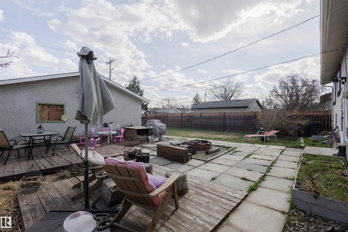 Spacious backyard featuring a wood-decked patio, stone-tiled patio, built-in fire pit, and privacy fencing - 5931 138 Avenue, Edmonton, AB - Outdoor With Deck Patio Veranda