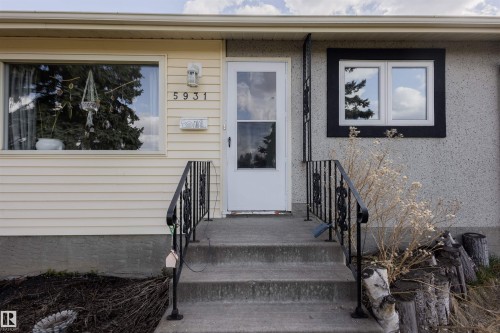 Exterior featuring a concrete porch with wrought iron railings, a white storm door, and contrasting siding and stucco finishes - 5931 138 Avenue, Edmonton, AB - Outdoor